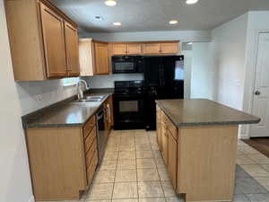 Kitchen featuring black appliances, dark countertops, a kitchen island, recessed lighting, and wood finish cabinetry
