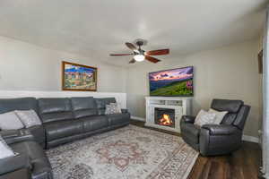 Living area with dark wood-type flooring, a glass covered fireplace, ceiling fan, and a textured ceiling