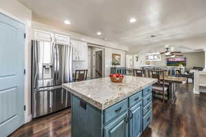 Dual tone kitchen with stainless steel fridge with ice dispenser, a kitchen island, decorative light fixtures, open floor plan, and two tone cabinetry