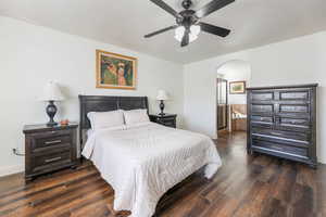 Bedroom featuring dark wood finished floors, ensuite bathroom, arched walkways, and a ceiling fan