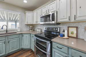 Two tone kitchen featuring stainless steel appliances, backsplash, two tone cabinets, dark wood-style floors, and light stone counters