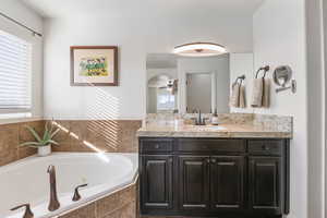 Bathroom with vanity, a tub with jets, healthy amount of natural light, and a ceiling fan