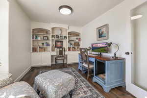 Office area featuring dark wood-style flooring, built in shelves, and built in desk