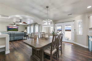 Dining space with french doors, dark wood-type flooring, a ceiling fan, hanging lights, and arched walkways