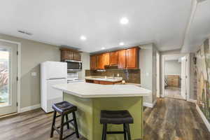 Kitchen with light countertops, white appliances, dark wood-style floors, a kitchen breakfast bar, and recessed lighting