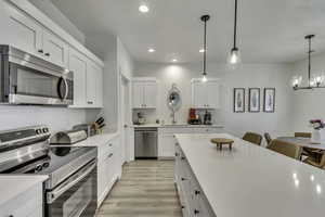 Kitchen with stainless steel appliances, white cabinetry, light wood-style floors, a breakfast bar area, and a chandelier