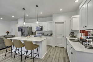 Kitchen featuring light wood-style flooring, stainless steel appliances, a kitchen island, pendant lighting, and a kitchen bar