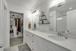 Bathroom with double vanity, a shower with door, a spacious closet, and light tile patterned floors
