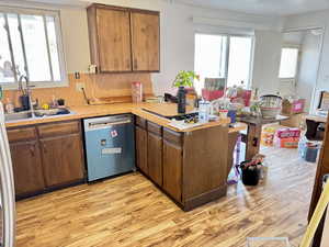 Kitchen featuring a peninsula, light countertops, dishwashing machine, and light wood-type flooring