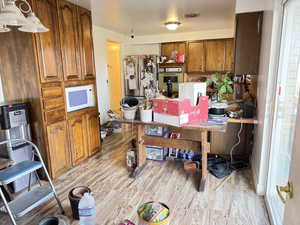 Kitchen featuring wood finish cabinetry, light wood-type flooring, white microwave, and freestanding refrigerator