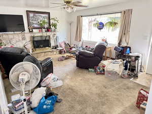 Living room featuring carpet, a ceiling fan, and a stone fireplace