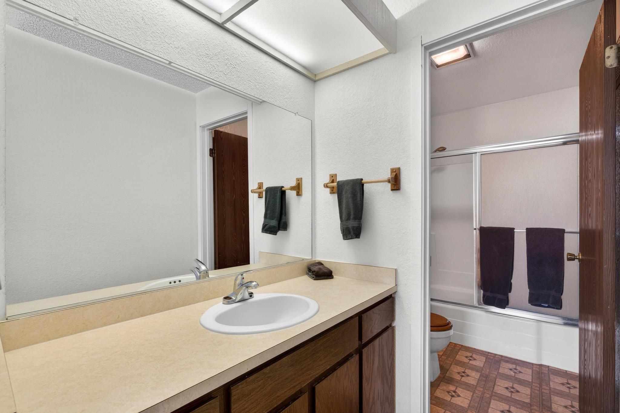 Full bathroom featuring bath / shower combo with glass door, vanity, dark floors, and a textured wall