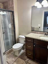 Full bath with stone tile flooring, vanity, and a shower stall