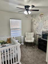 Bedroom with a crib, dark colored carpet, a textured ceiling, and a ceiling fan