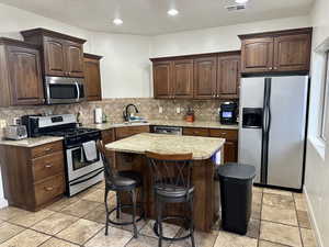 Kitchen featuring stainless steel appliances, a kitchen island, light stone countertops, a kitchen breakfast bar, and dark wood finish cabinets
