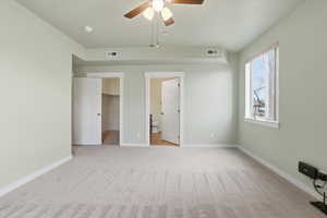 Primary bedroom suite with a spacious walk-in closet, light colored carpet, ceiling fan, and ensuite bath