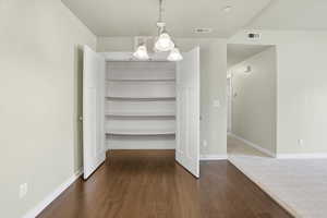 Unfurnished dining area with hanging lights, dark wood-style floors, and a large pantry.