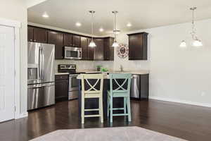Kitchen with light countertops, stainless steel appliances, dark wood finish cabinetry, a kitchen bar, and a kitchen island