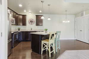 Kitchen featuring dark wood finish cabinetry, a kitchen bar, stainless steel appliances, dark wood finished floors, and a kitchen island