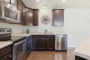 Kitchen featuring stainless steel appliances, dark wood finish cabinets, light countertops, wood finish floors, and recessed lighting