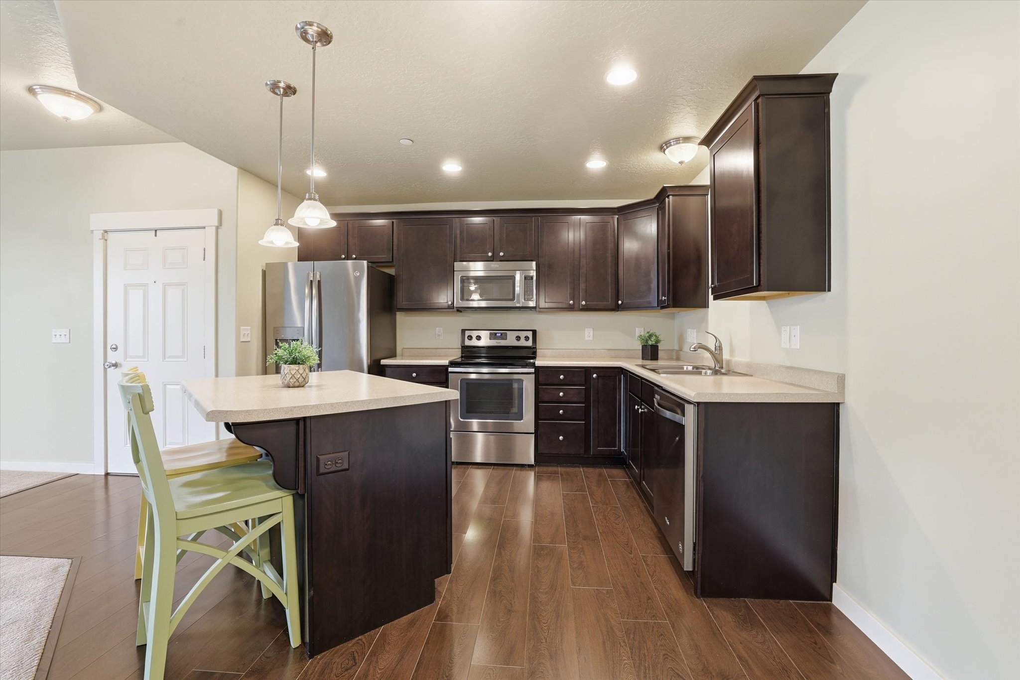 Kitchen featuring dark wood finish cabinets, stainless steel appliances, hanging light fixtures, dark wood-style flooring, and light countertops