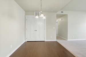 Unfurnished dining area with hanging lights and dark wood-style floors and large pantry closet