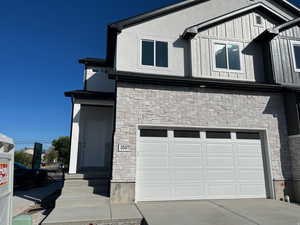 View of front of home featuring stone siding, an attached garage, concrete driveway, and board and batten siding