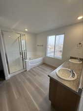 Bathroom with a garden tub, double vanity, a shower stall, light wood-type flooring, and recessed lighting