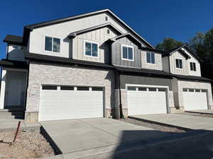 View of front of home with stone siding, concrete driveway, a garage, board and batten siding, and stucco siding