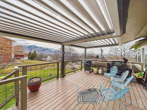 Wooden deck featuring a lawn, a mountain view, and a grill area with pergola