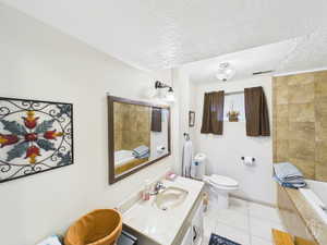 Bathroom with vanity, light tile patterned floors, a textured ceiling, and tiled shower / bath combo