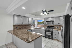 Kitchen featuring stainless steel appliances, dark stone countertops, ceiling fan, light tile patterned floors, and a raised ceiling