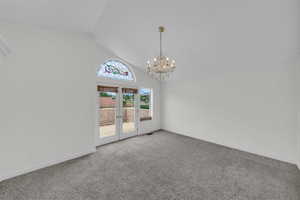 Carpeted empty room with a chandelier and lofted ceiling