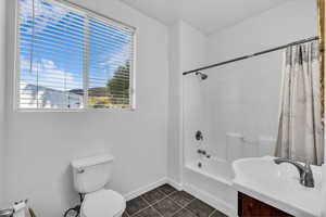 Bathroom featuring shower / bathtub combination with curtain, vanity, and dark tile patterned floors