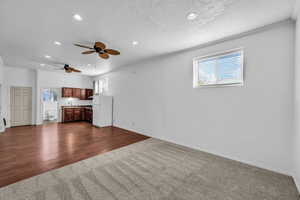 Unfurnished living room with healthy amount of natural light, dark colored carpet, recessed lighting, ceiling fan, and dark wood-style flooring