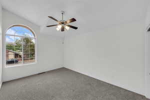 Carpeted spare room featuring ceiling fan and lofted ceiling