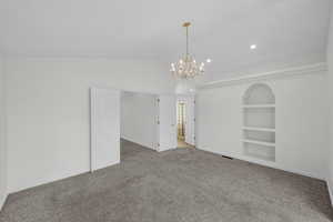 Carpeted spare room with built in shelves, lofted ceiling, and a chandelier