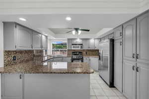 Kitchen with a peninsula, stainless steel fridge with ice dispenser, range with gas cooktop, a raised ceiling, and light tile patterned floors