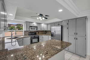 Kitchen featuring dark stone counters, black gas range oven, stainless steel refrigerator with ice dispenser, a tray ceiling, and a peninsula
