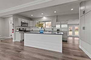 Kitchen with stainless steel appliances, dark stone counters, a center island, dark wood-style floors, and recessed lighting