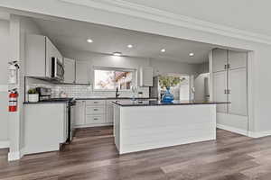 Kitchen featuring stainless steel appliances, dark stone countertops, white cabinetry, backsplash, and dark wood finished floors