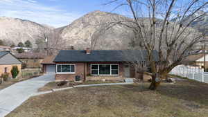Ranch-style home featuring concrete driveway, brick siding, a chimney, a mountain view, and a shingled roof