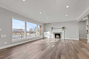Unfurnished living room featuring a tiled fireplace, wood finished floors, crown molding, and recessed lighting