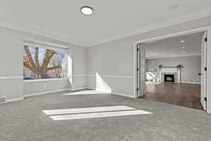 Spare room featuring a tiled fireplace, carpet floors, and crown molding
