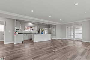 Kitchen with open floor plan, dark countertops, a center island, ornamental molding, and light wood-style floors