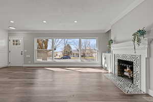 Unfurnished living room featuring a tiled fireplace, wood finished floors, crown molding, and a textured ceiling