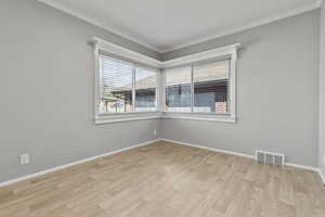 Empty room with light wood-style floors, plenty of natural light, and ornamental molding