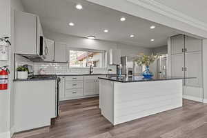 Kitchen featuring dark stone countertops, stainless steel appliances, backsplash, dark wood-type flooring, and recessed lighting