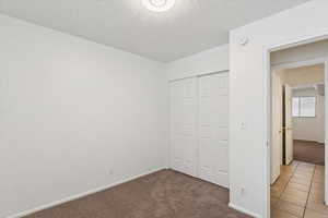 Unfurnished bedroom with dark colored carpet, a closet, a textured ceiling, and dark tile patterned flooring