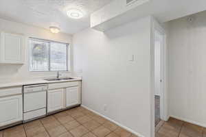 Kitchen featuring white cabinetry, a textured ceiling, dishwasher, and light countertops